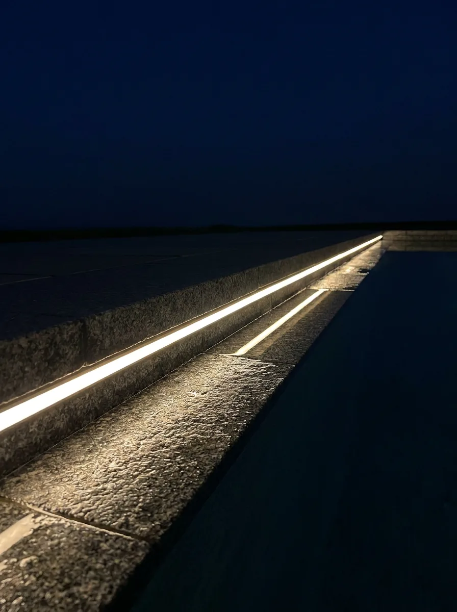 Elevated view of a contemporary Australian backyard at deep dusk — path edges, garden beds, pool surround and bench underglow traced in continuous warm 2700K LED strip light, like a lighting plan come to life.